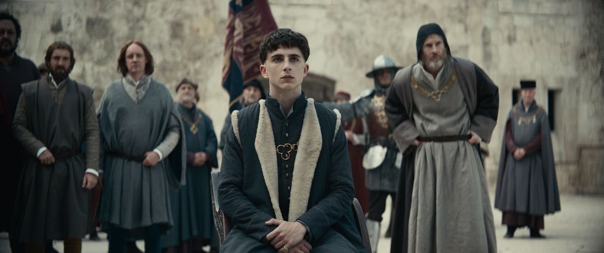 Henry (Chalamet) sits in front of a group of his subjects.