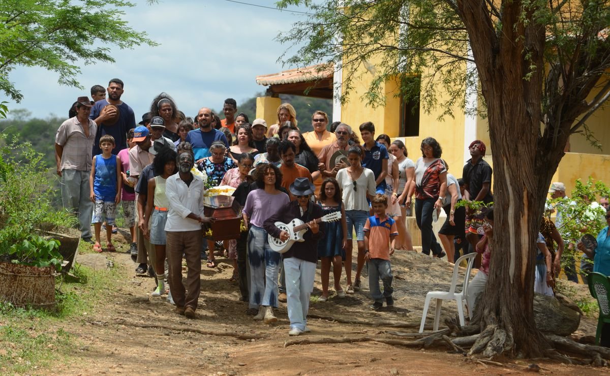A man with a white guitar leads a funeral procession through the small Brazilian town of Bacurau, as the locals carry a wooden coffin from a bright yellow house to the local cemetery.