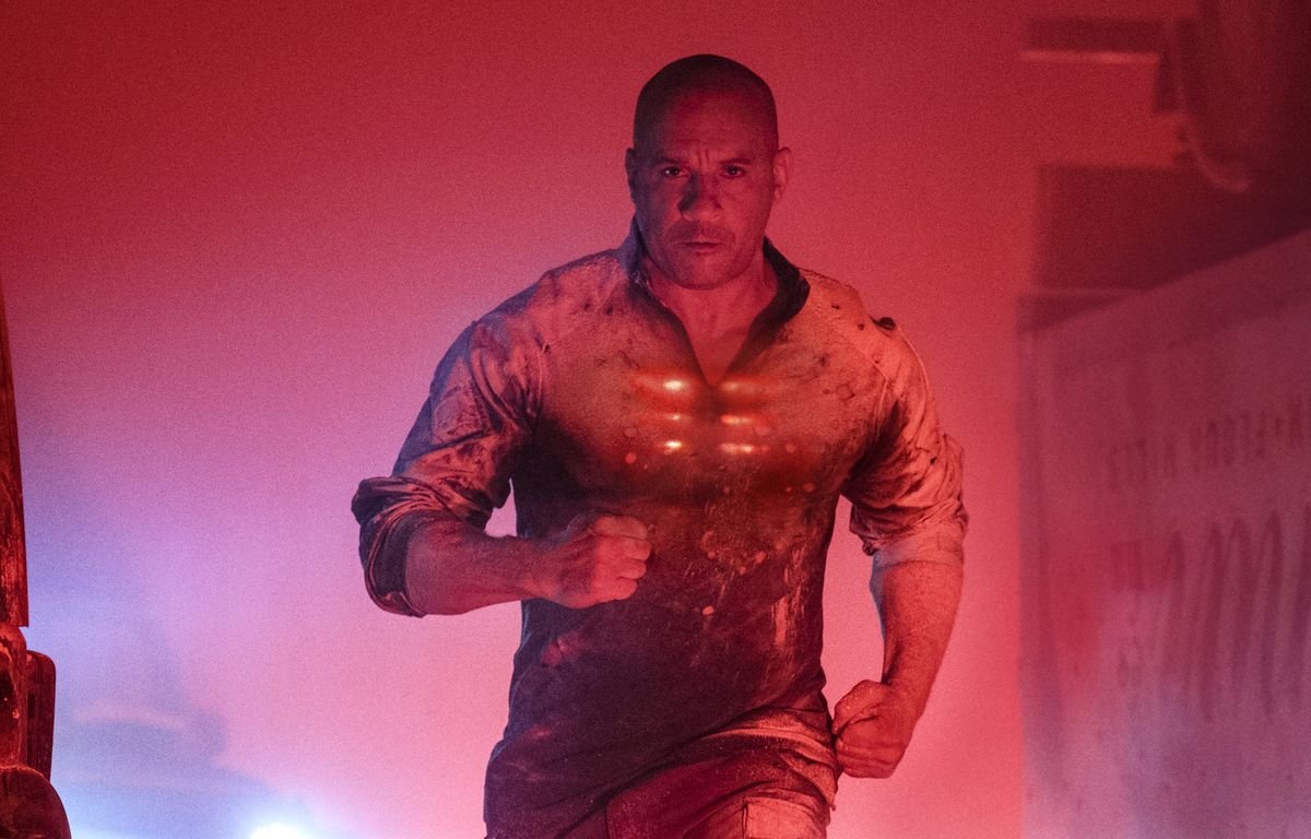 Vin Diesel runs toward the camera, looking determined, his chest glowing red, in a red-lit photo.