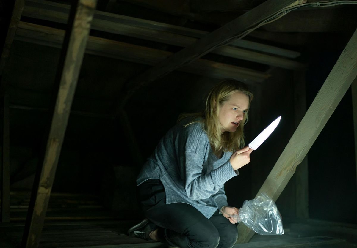 A distressed-looking blonde woman kneels in a dark, unfinished attic, clutching a shining knife in one hand and a crumpled plastic bag in the other.