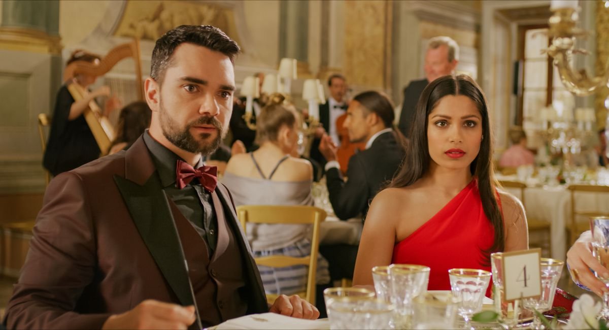 Gross power couple Chaz (Allan Mustafa) and Amanda (Freida Pinto), sitting at a wedding reception table, glare disbelievingly at something offscreen.
