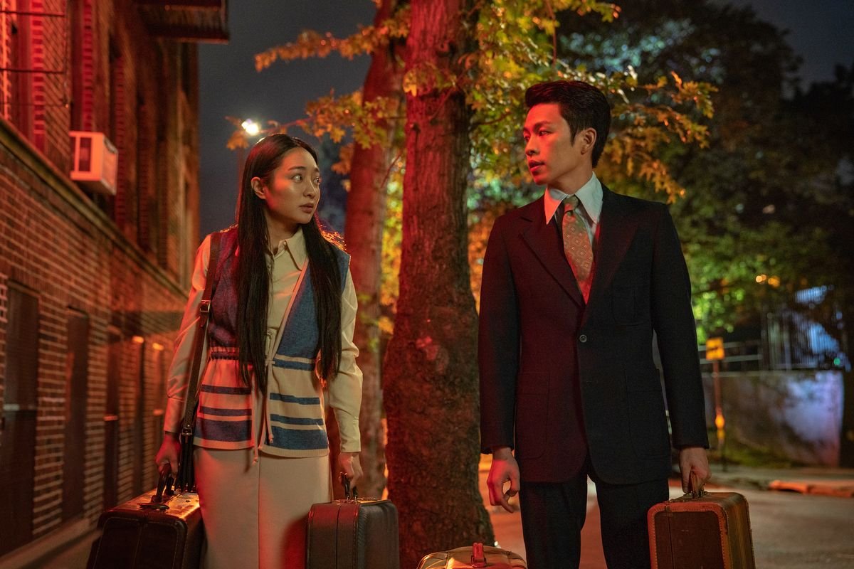 a man and woman stand holding suitcases