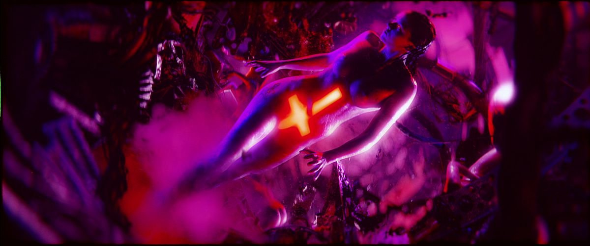 A naked woman, lit in purple, with a glowing red inverted cross covering her stomach and groin, stands in an abstract purple landscape, surrounded by mist and tree-like structures