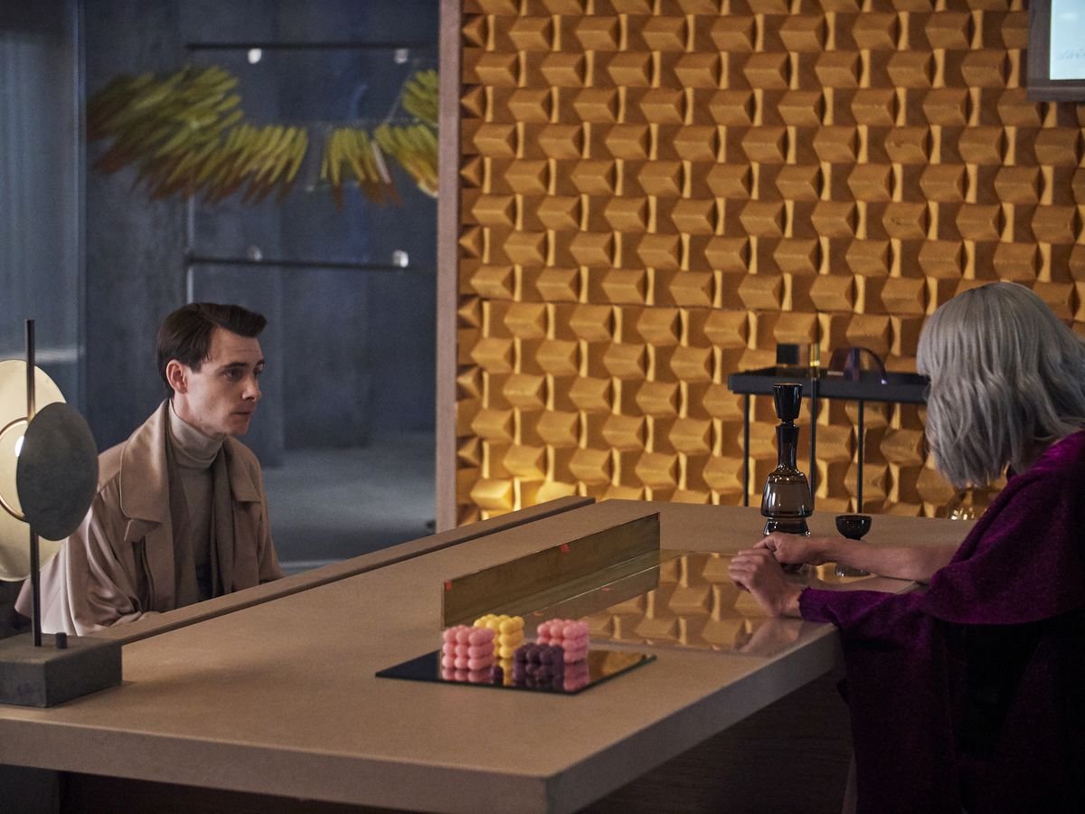 Harry Lloyd, looking nervous, sits opposite a broad table from Hannah John-Kamen in Brave New World.