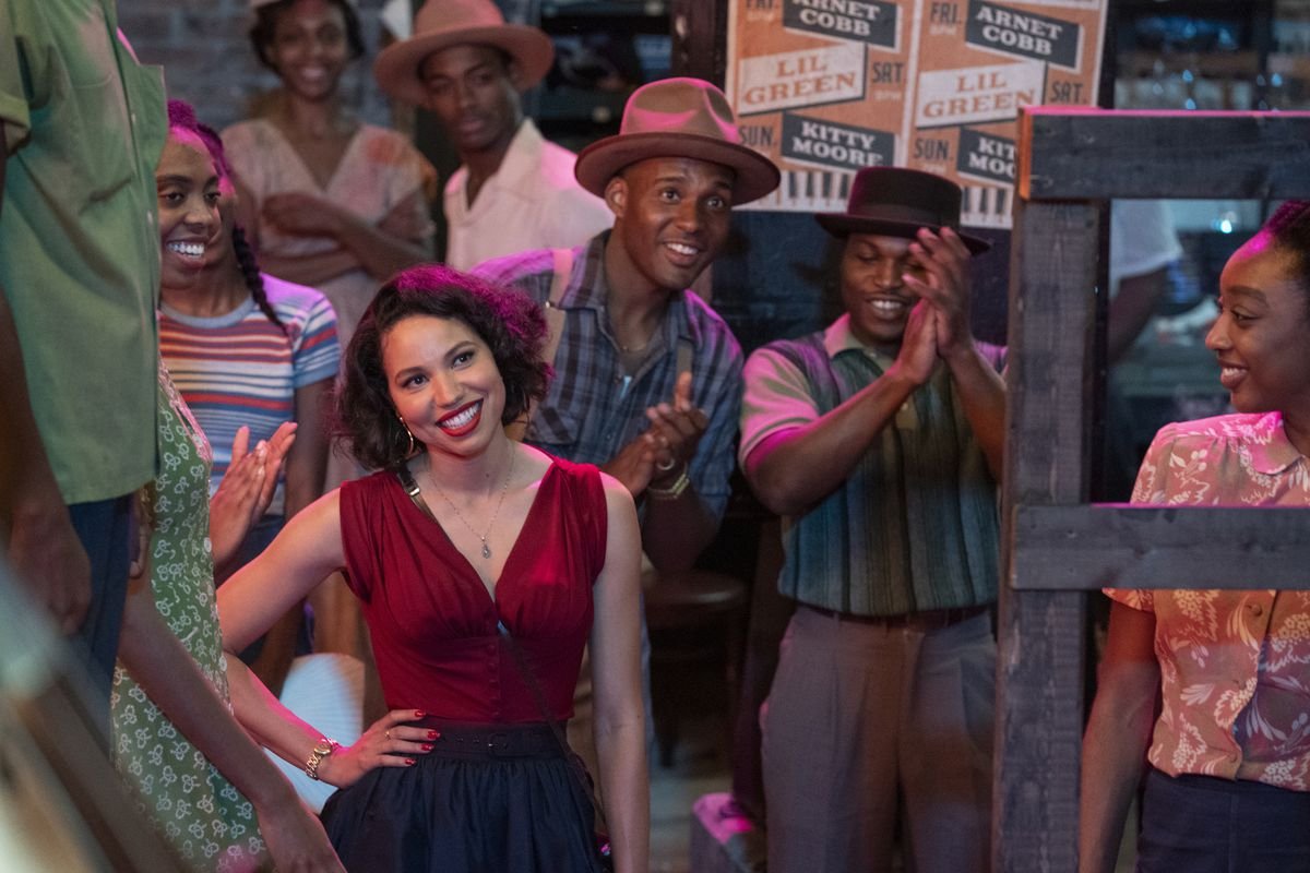 Jurnee Smollett stands smiling in a crowd of applauding people in Lovecraft Country.
