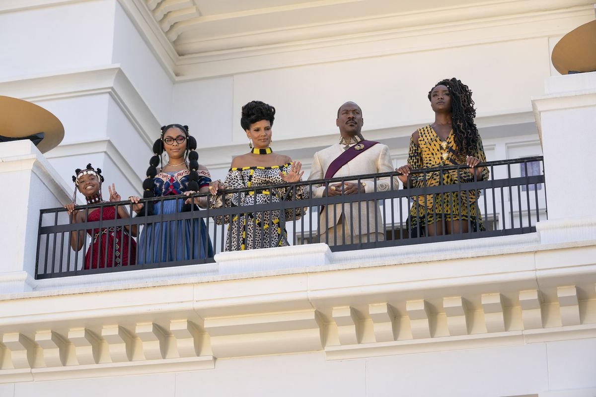 Prince Azeem (Eddie Murphy) and his family, played by Akiley Love, Bella Murphy, KiKi Layne, and Shari Headley, stand on a balcony looking down in Coming 2 America