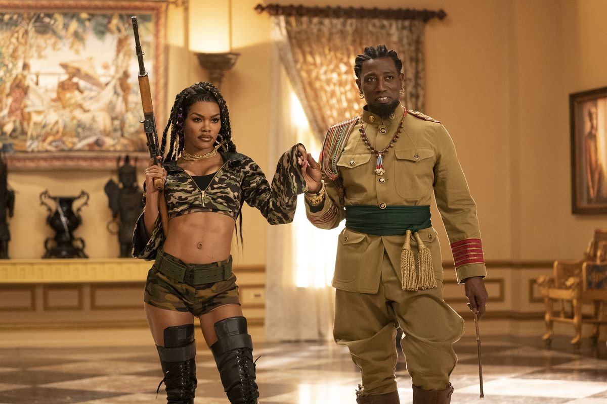 Teyana Taylor, holding a rifle and wearing a belly-baring camo outfit, holds Wesley Snipes’ hand in Coming 2 America