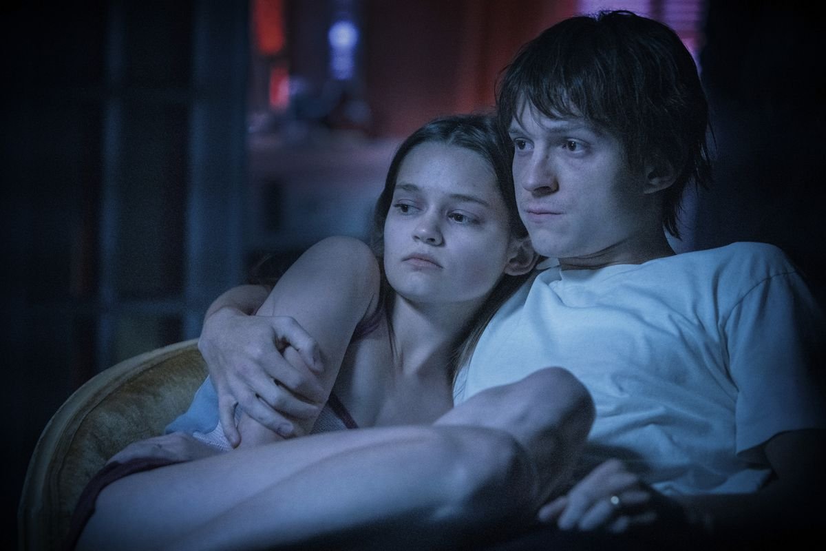 Cherry (Tom Holland) and his wife Emily (Ciara Bravo), bathed in blue light, sit strung out on the couch after shooting up heroin