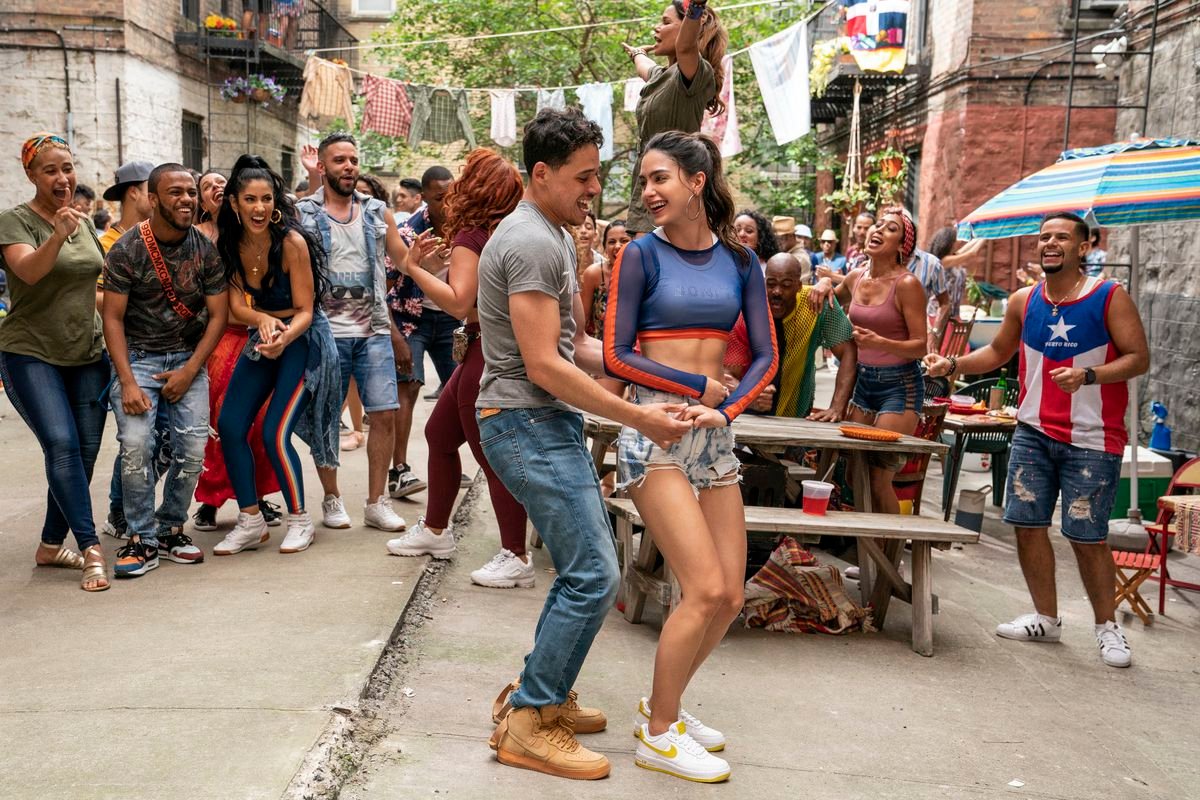 a man and woman dance in front of a picnic table as their friends cheer them on in In the Heights