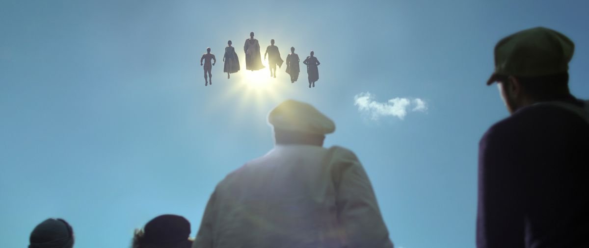 A crowd seen from behind look upward at six hovering superheroes eclipsing the sun in Jupiter’s Legacy