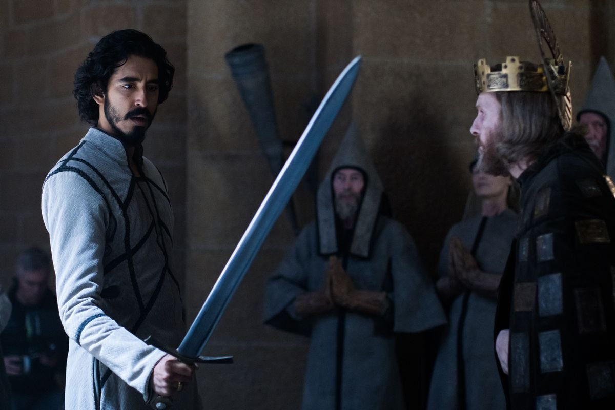 Dev Patel as Gawain holds up Excalibur in court in David Lowery’s The Green Knight