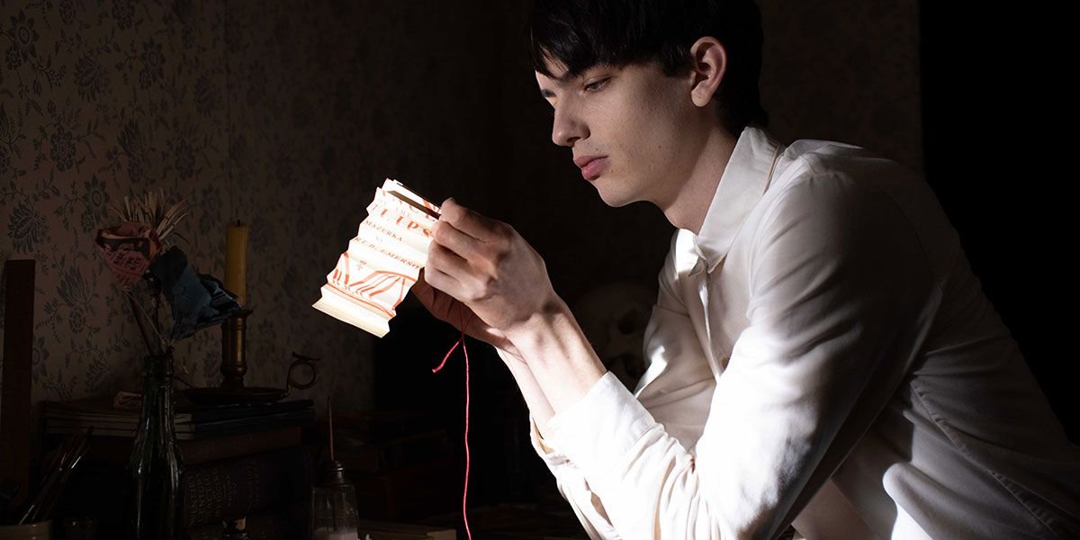 Kodi Smit-McPhee sews red thread through a white cloth in a darkened room in The Power of the Dog