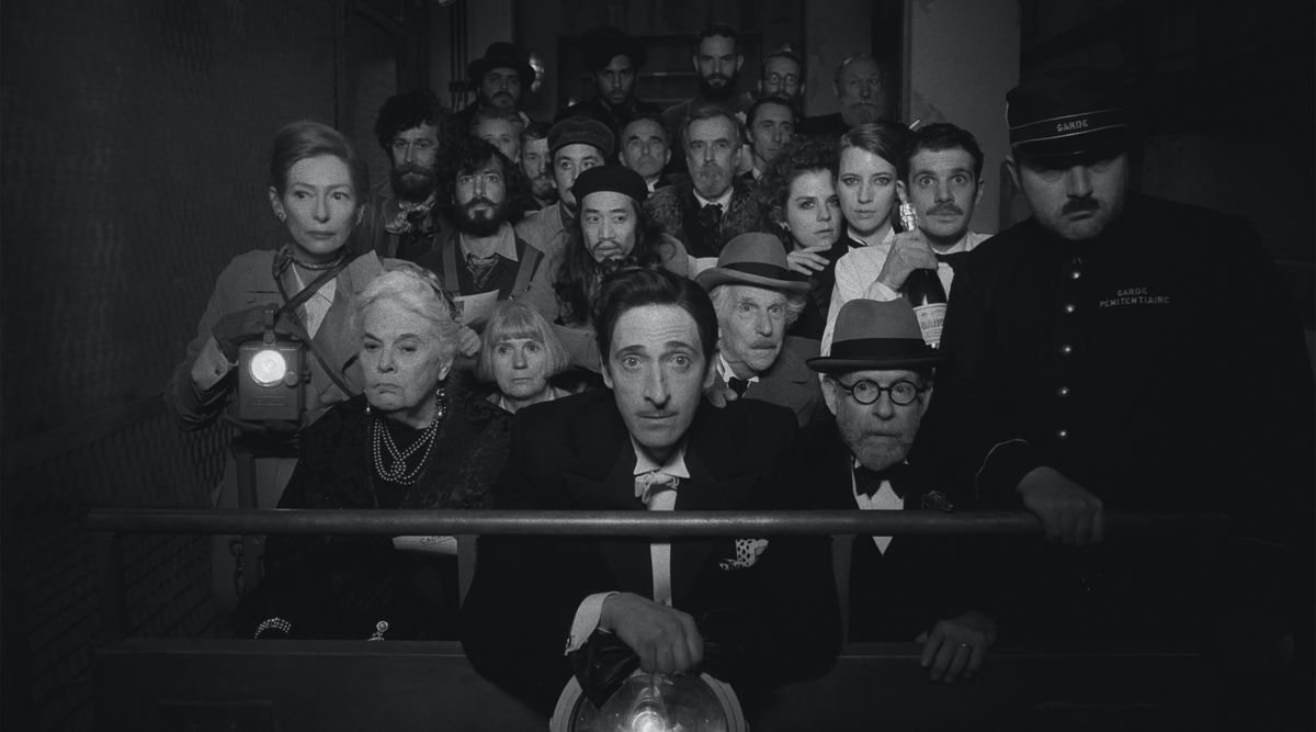 Tilda Swinton, Lois Smith, Adrien Brody, Henry Winkler, Bob Balaban, and a crowd of others pack into a train car and stare into the camera in Wes Anderson’s The French Dispatch.