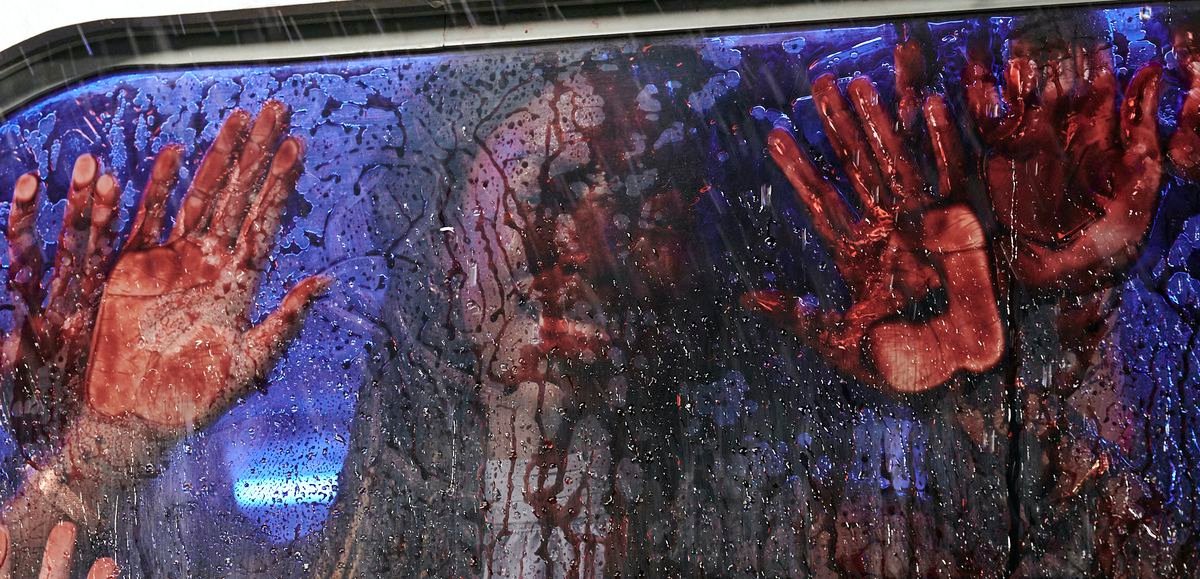 A bloody face and four bloody hands press up against the interior of an incredibly bloody car window in the 2022 Texas Chainsaw Massacre