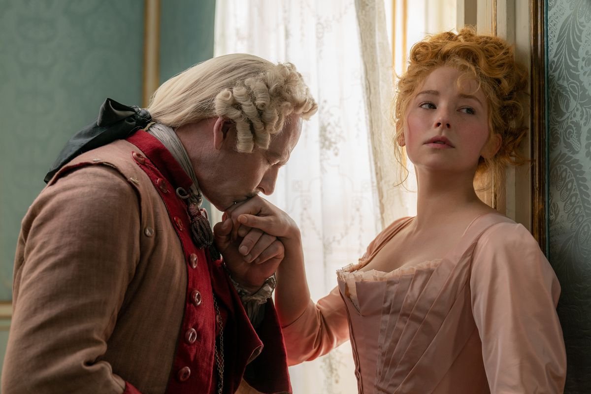 Ben Mendelsohn as De Guiche, in a curled and ribboned wig, kisses the hand of clearly unwilling Haley Bennett as Roxanne in Joe Wright’s Cyrano