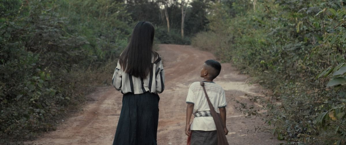 A young Lao boy and his ghost companion walk along a dirt path through the forest in Mattie Do’s The Long Walk