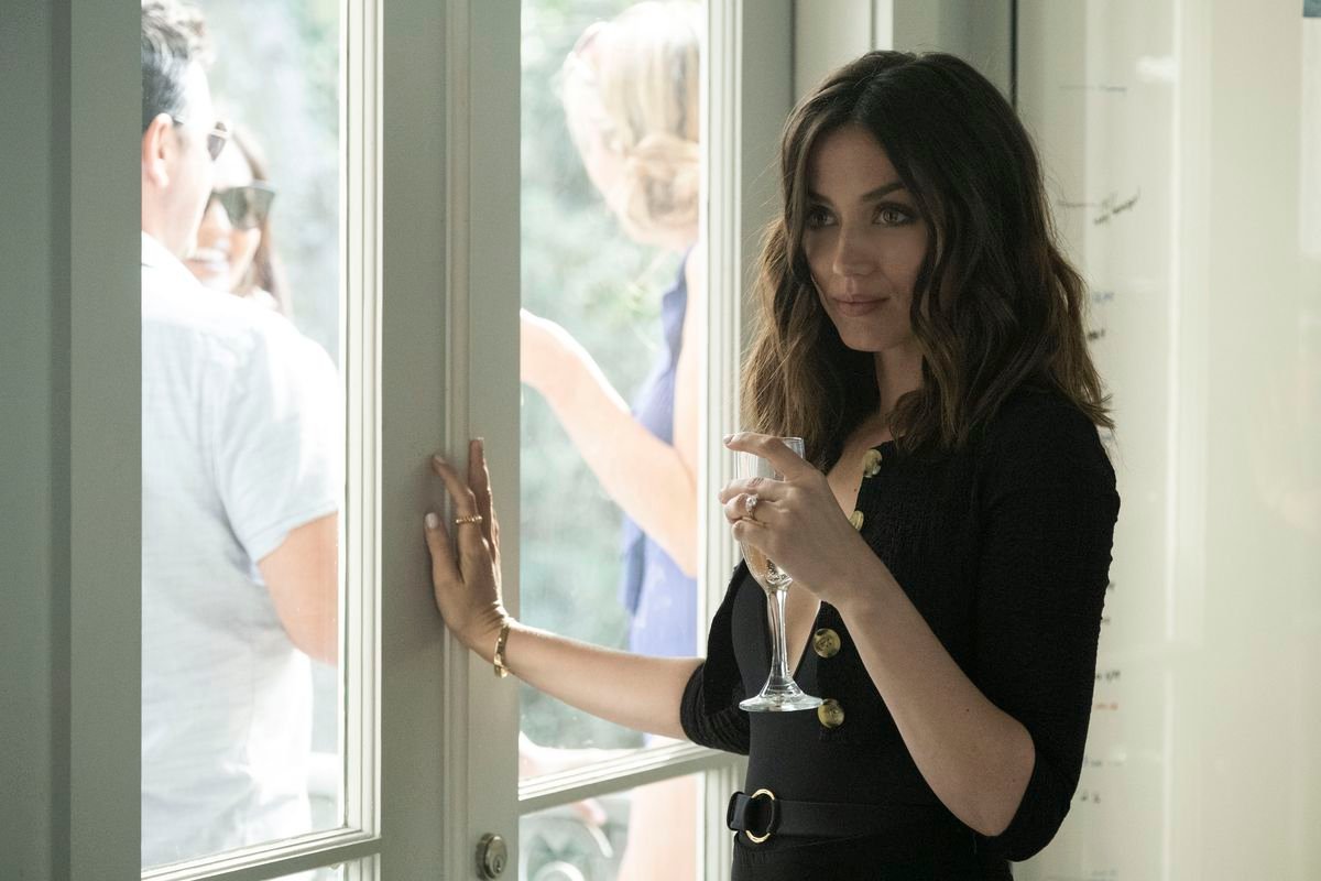 Ana de Armas stands seductively by a window, glass in hand