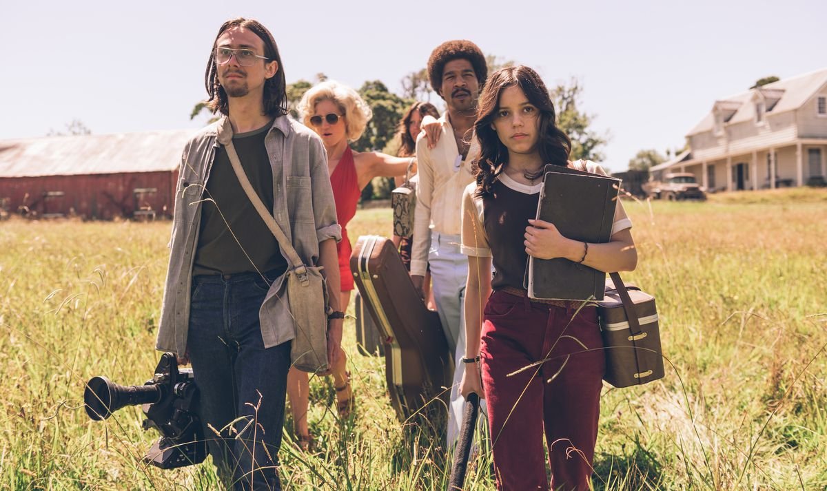 The doomed crew of X walks through tall grass, film equipment in hand