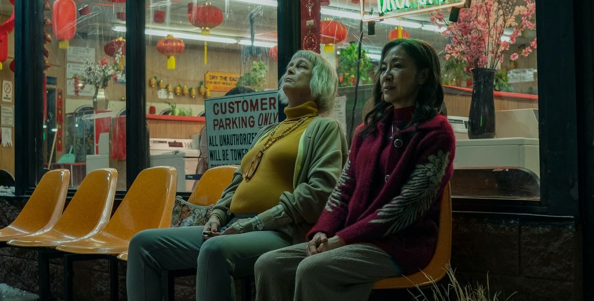 Jamie Lee Curtis and Michelle Yeoh sit wearily outside of a laundromat at night in Everything Everywhere All At Once