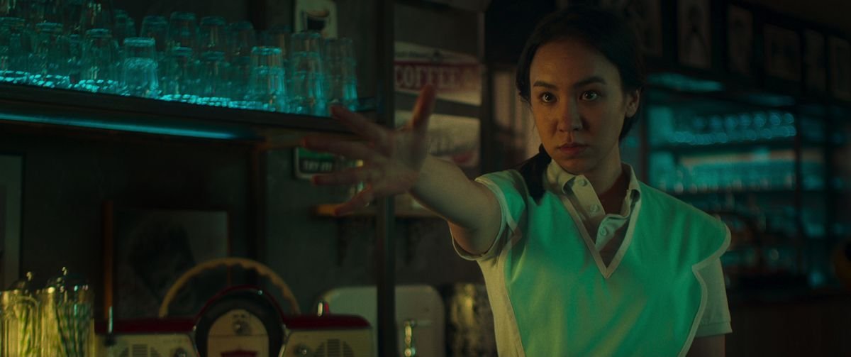 Ioanna Kimbook as Grace makes a dramatic extended-hand gesture in another dimly lit, grimy scene from Netflix’s Choose or Die.