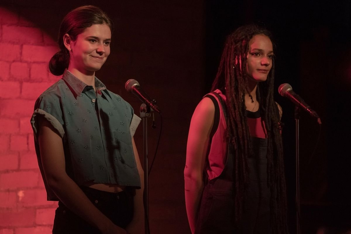 Frances and Bobbi standing on stage in front of microphones in a red light