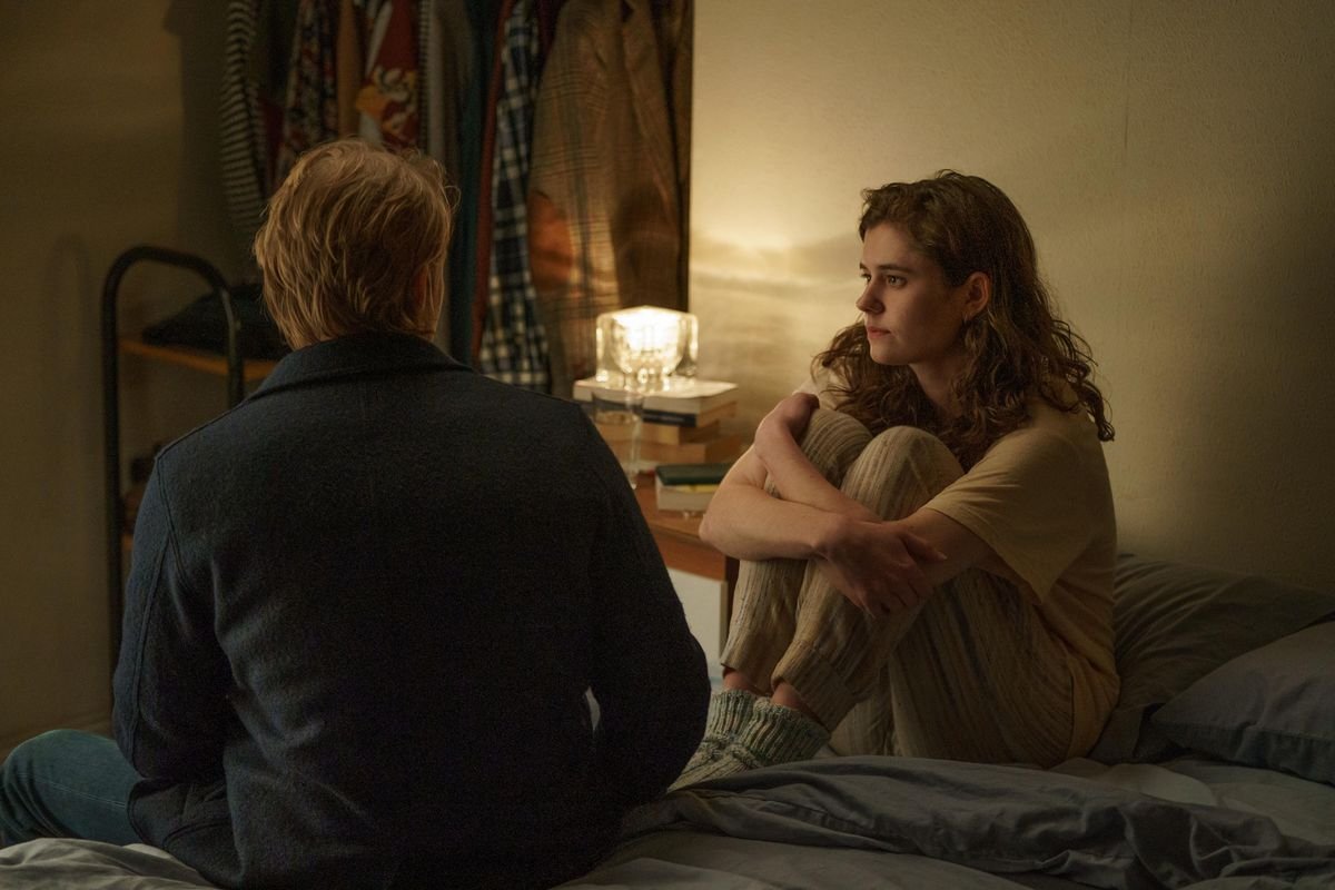 Frances hugging her knees to her chest on her bed and Nick sitting on the bed looking at her, his back to the camera