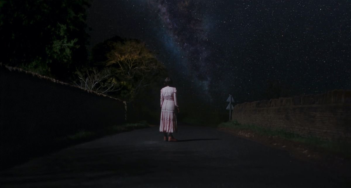 Jessie Buckley, in a long pink dress, stands outside at night under a vast canopy of stars in Alex Garland’s Men.