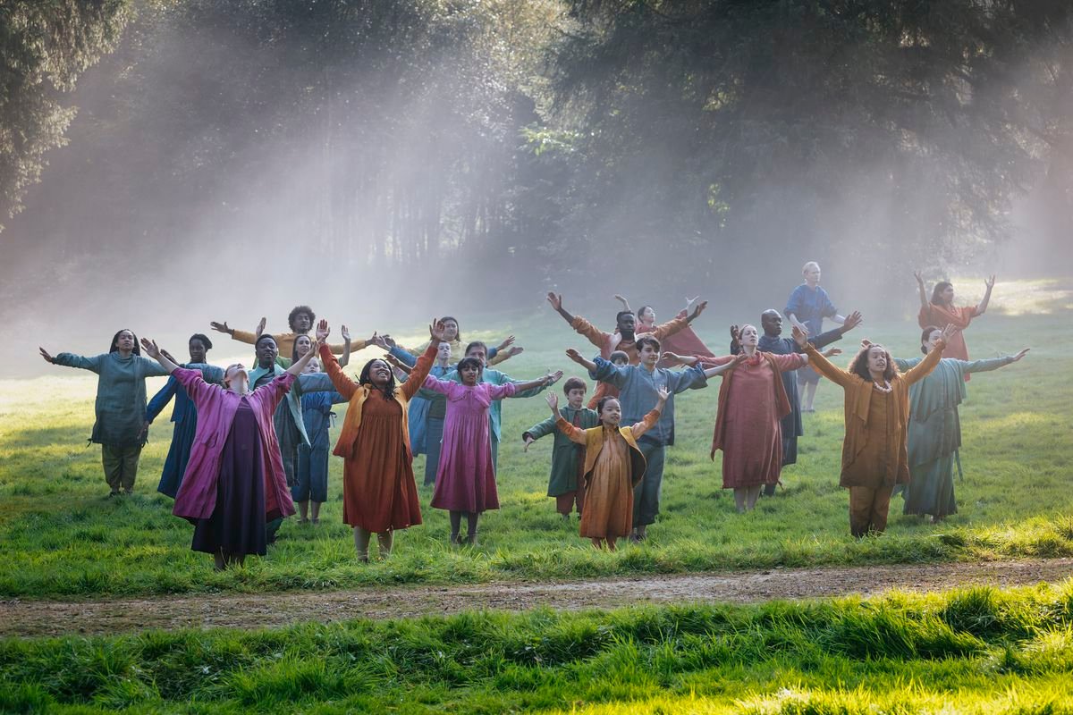 A group of people in colorful clothes raising their arms up and open in a foggy grass clearing