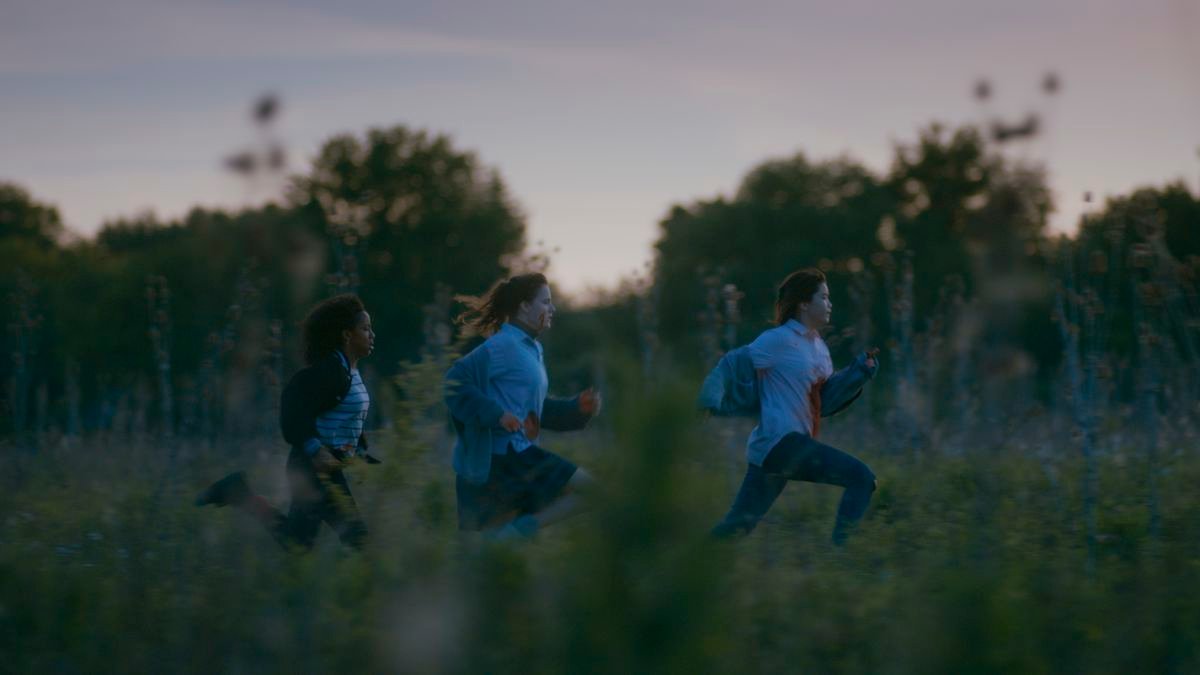 Three of the Paper Girls running through a field