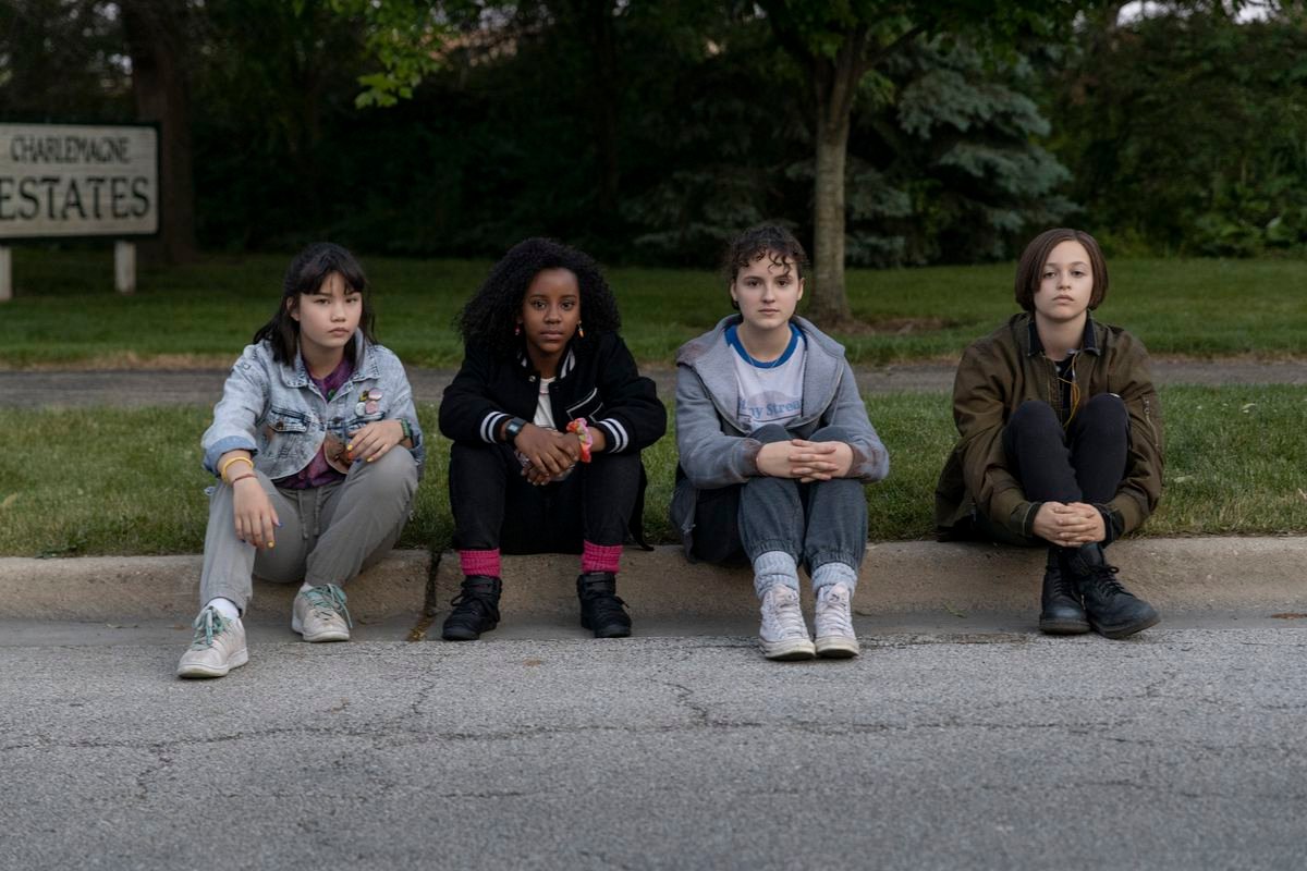 The four Paper Girls sitting on a curb