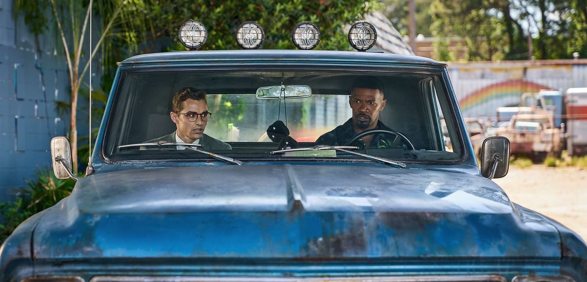 Dave Franco and Jamie Foxx sit together in a rusty blue truck in Day Shift