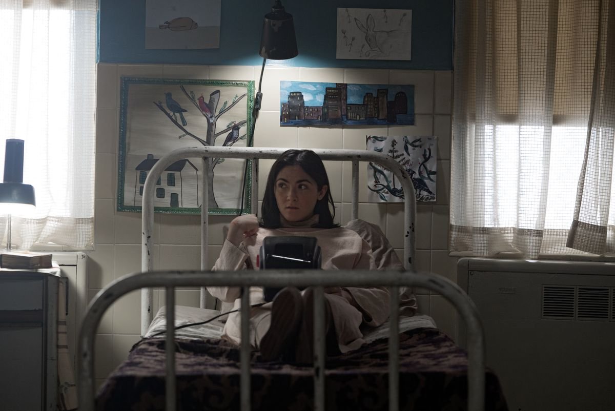 Isabelle Fuhrman as Esther in Orphan: First Kill sitting on a bed reading a book