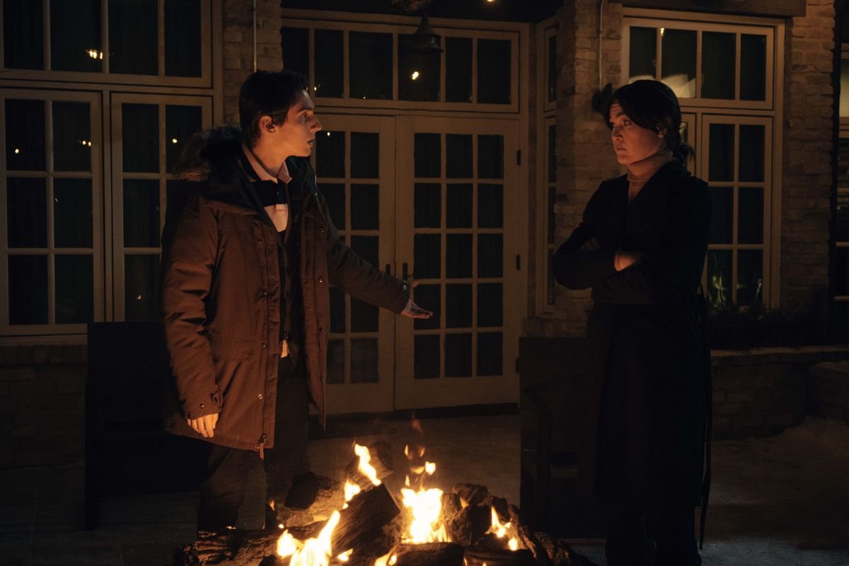 Matthew Finlan and Julia Stiles argue with each other in front of a fire in Orphan: First Kill