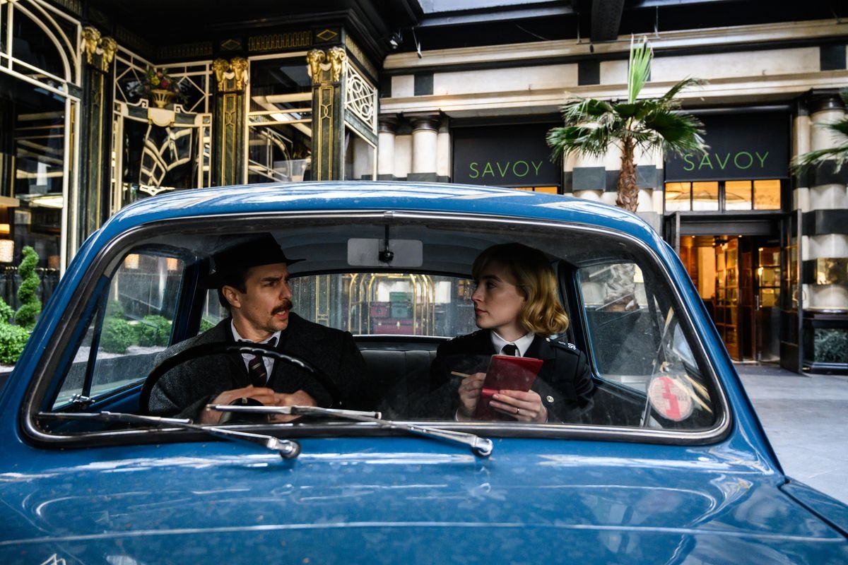 Inspector Stoppard (Sam Rockwell) and Constable Stalker (Saoirse Ronan) talk in a small blue police car outside the Savoy Hotel