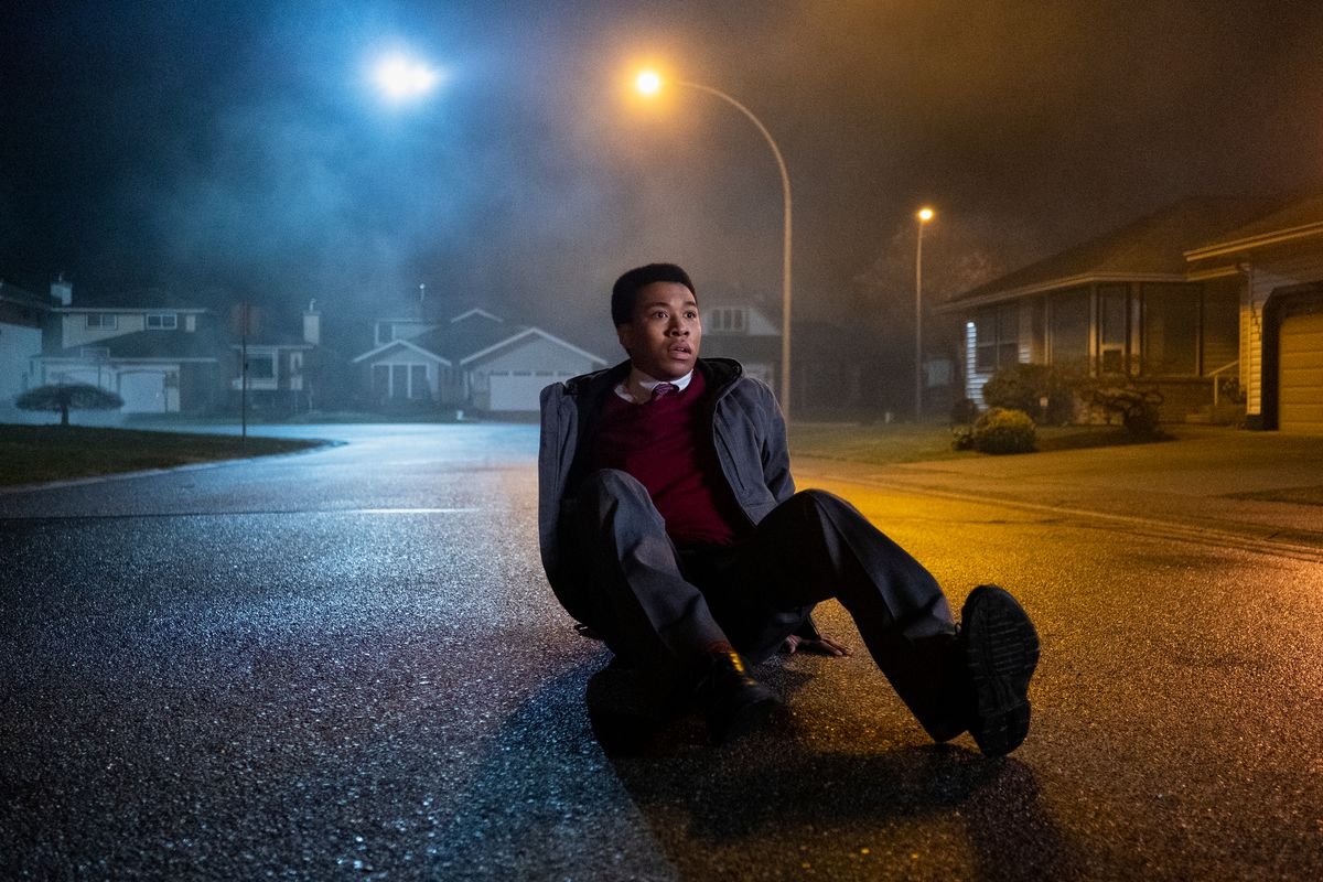 A Midnight Club character sitting on the ground looking very startled at something off-camera; he’s sitting on the street of a suburban cul de sac