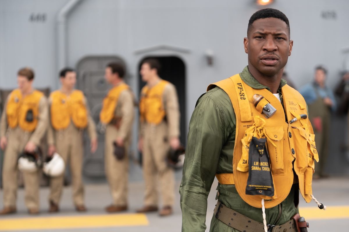 Jesse Brown (Jonathan Majors) stands on the deck of a ship in Navy fighter-pilot gear and an inflatable life vest in Devotion