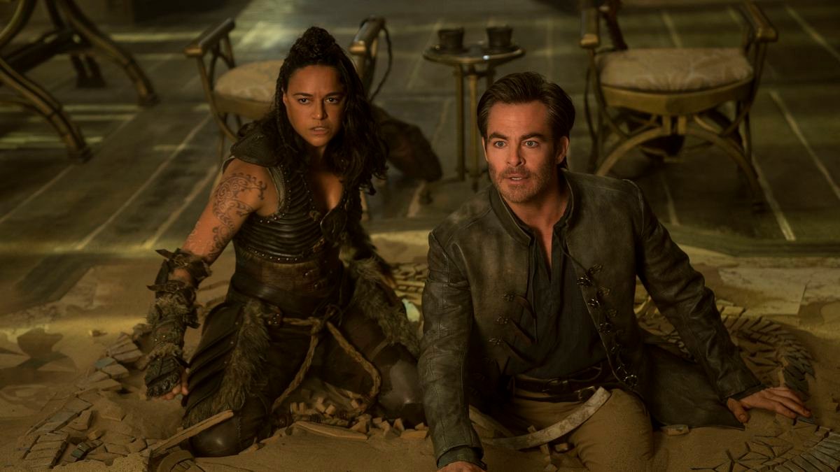 Barbarian Holga (Michelle Rodriguez) and bard Edgin (Chris Pine) kneel awkwardly in sand and shattered tiles in front of several chairs in Dungeons & Dragons: Honor Among Thieves