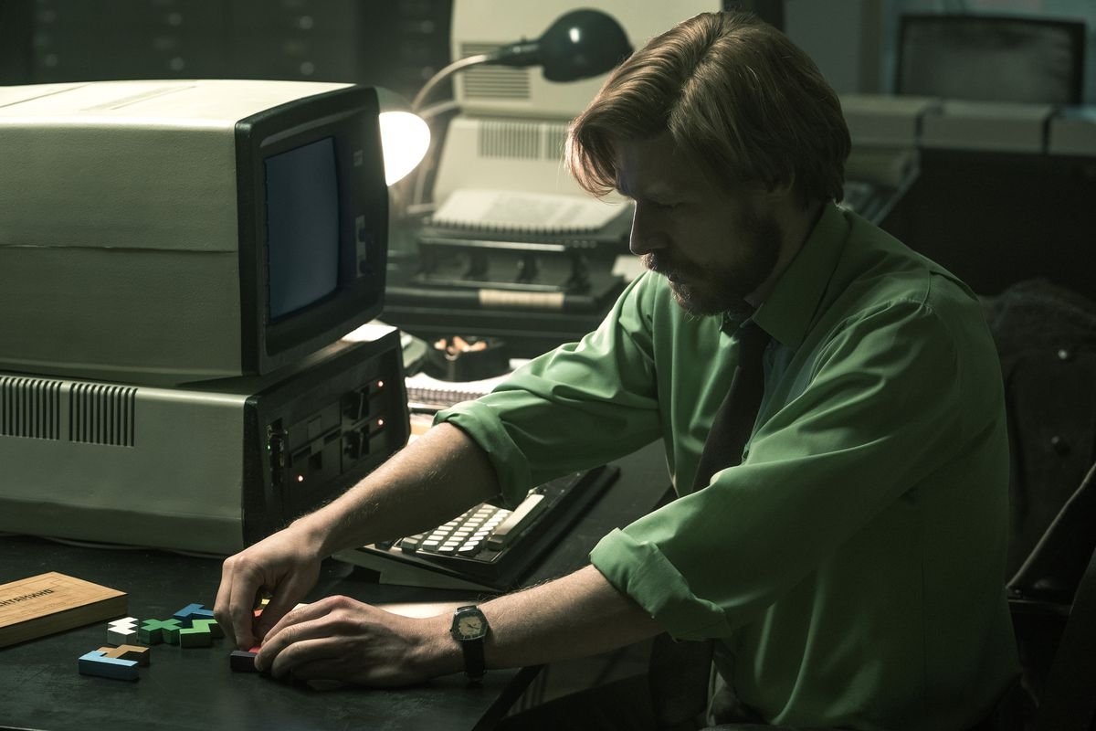 Nikita Efremov, as Alexey Pajitnov, puzzles over pentominoes pieces at his computer workstation in a still from the movie Tetris