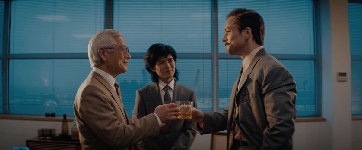 Togo Igawa as Hiroshi Yamauchi and Taron Egerton as Henk Roger toast each other in a still from the movie Tetris.