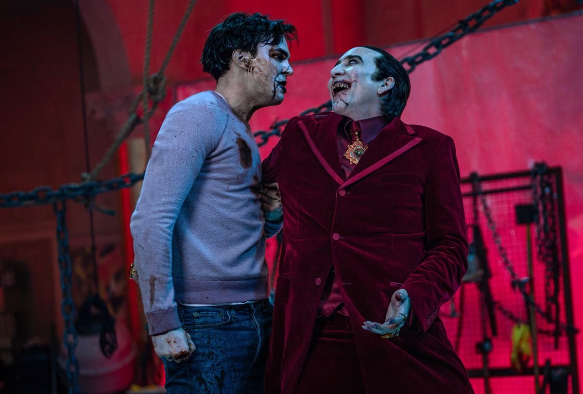 Renfield (Nicholas Hoult), in a bloody sweatshirt and with blackish blood all over his face, glares at a cackling, bloody-mouthed Dracula (Nicolas Cage) in Renfield