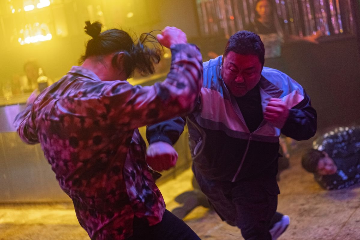 A man wearing a club shirt goes flying as Ma Dong-seok punches him in the ribs in a club in The Roundup: No Way Out.