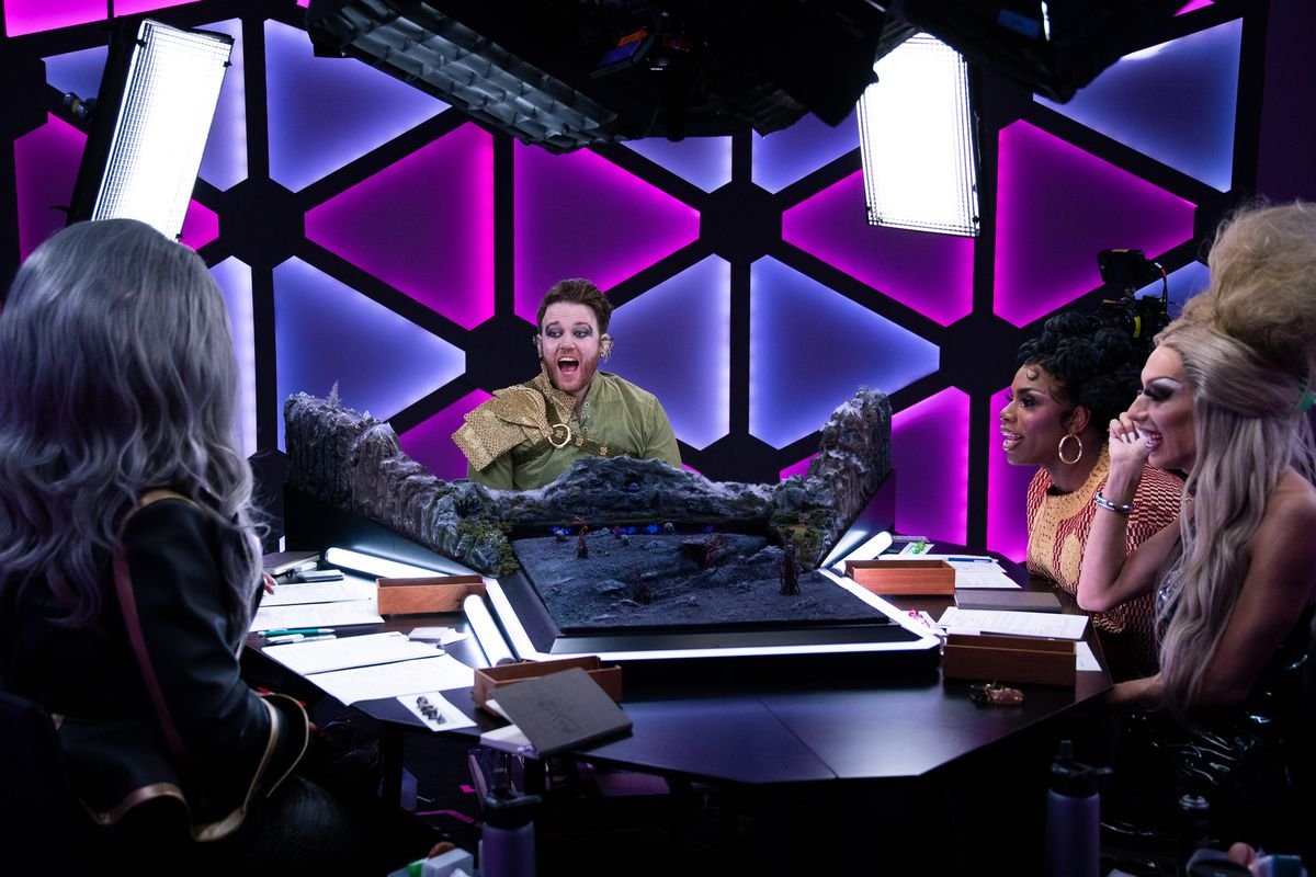 Brennan Lee Mulligan grins against the dome, turned purple and lavender. Meanwhile the cast of Dungeons and Drag Queens looks on, laughing.