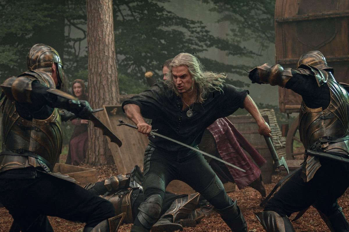 Geralt wields a sword and axe as soldiers attack him on each side in a fight scene from The Witcher season 3