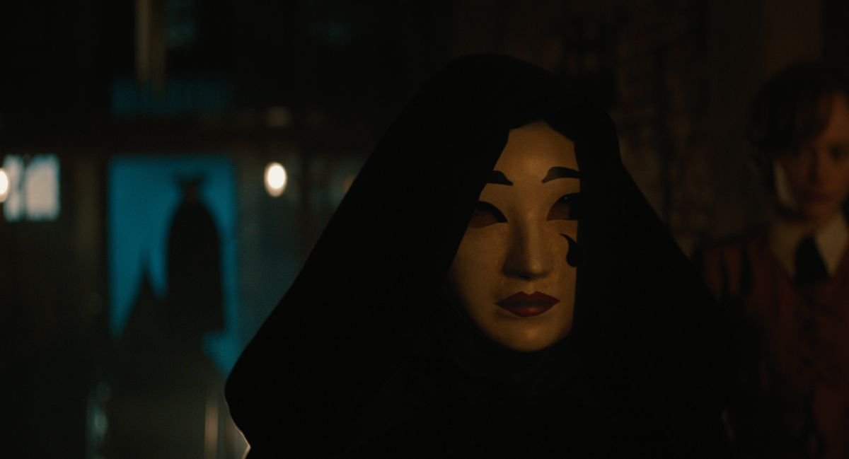 A hooded figure wears a creepy Venetian carnival mask