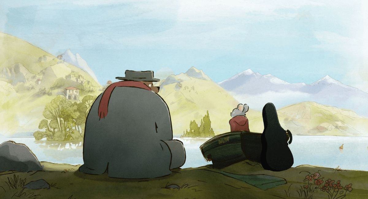 Ernest, a hulking bear in shapeless grey coat, flat grey hat, and red scarf, sits next to Celestine, a small grey mouse in a red hooded cloak, beside a pastoral body of water in Ernest & Celestine: A Trip to Gibberitia