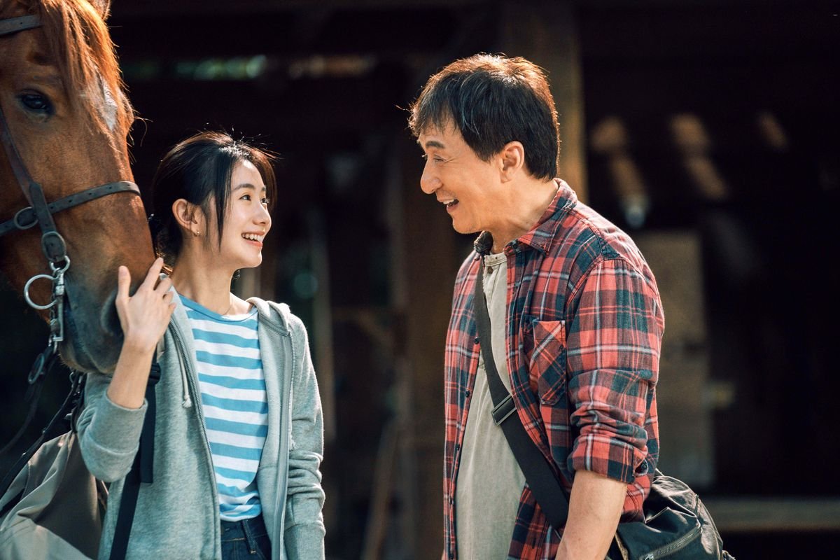Jackie Chan and Haocun Liu smile at each other as she holds a horse’s muzzle in Ride On.