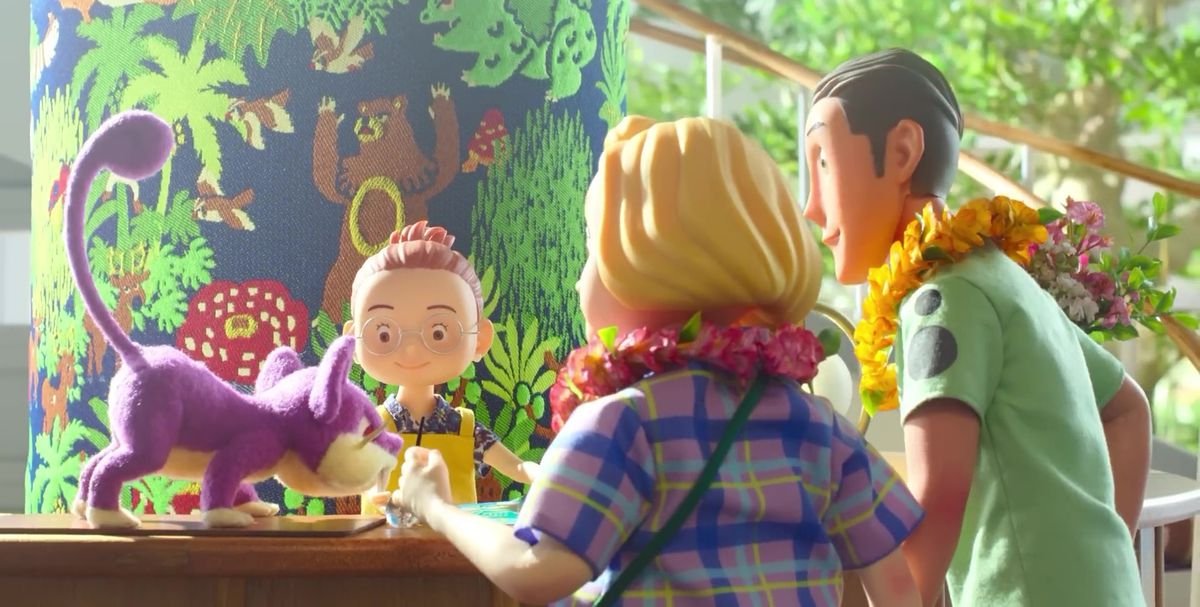 A still from the stop-animation show Pokemon Concierge. Three human visitors look over a piece of paper on a counter as a Ratata looks over at it with them while standing on the counter. The Ratata is made with a fuzzy, felt-like material.