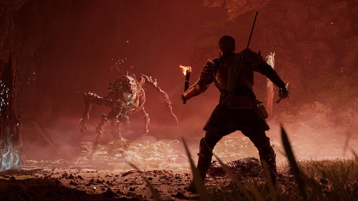 Red, holding a torch and a sword, faces a gruesome creature in a misty, red-hued environment in Banishers: Ghosts of New Eden