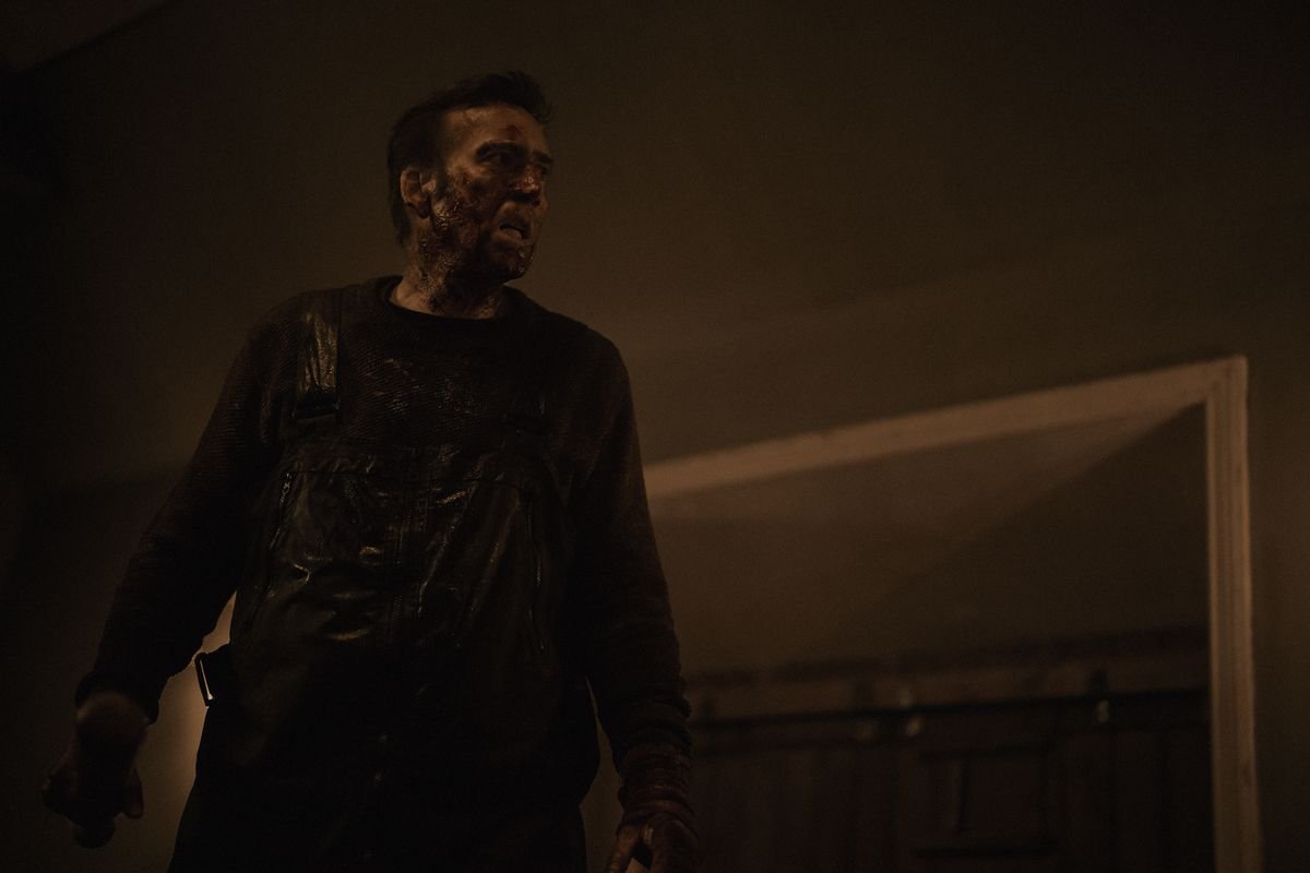 Paul (Nicolas Cage) stands in in a dark room looking grim in Arcadian