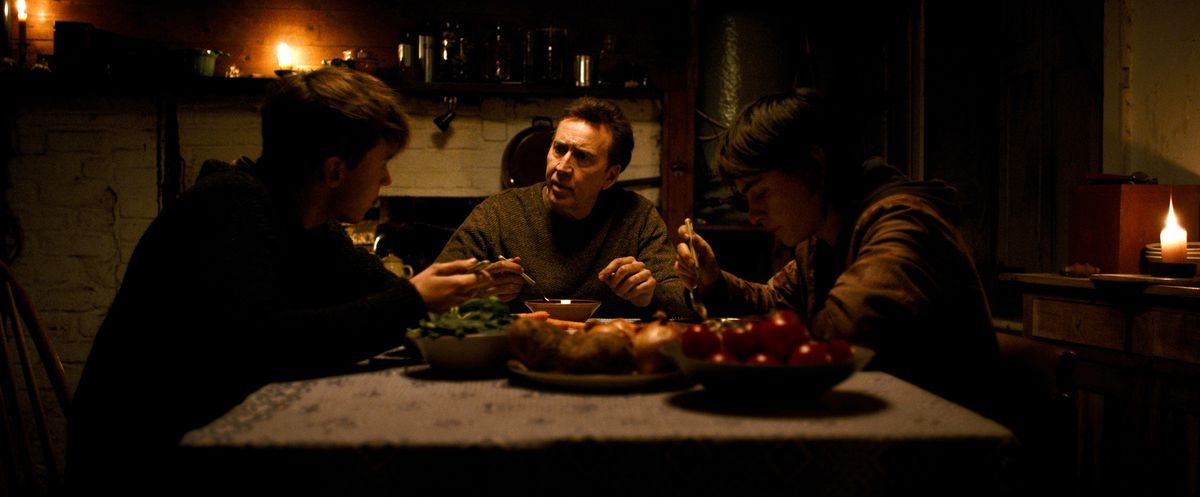 Paul (Nicolas Cage) and 15-year-old twins Thomas (Maxwell Jenkins) and Joseph (Jaeden Martell) sit at the dinner table in a bleak, dark room in Arcadian